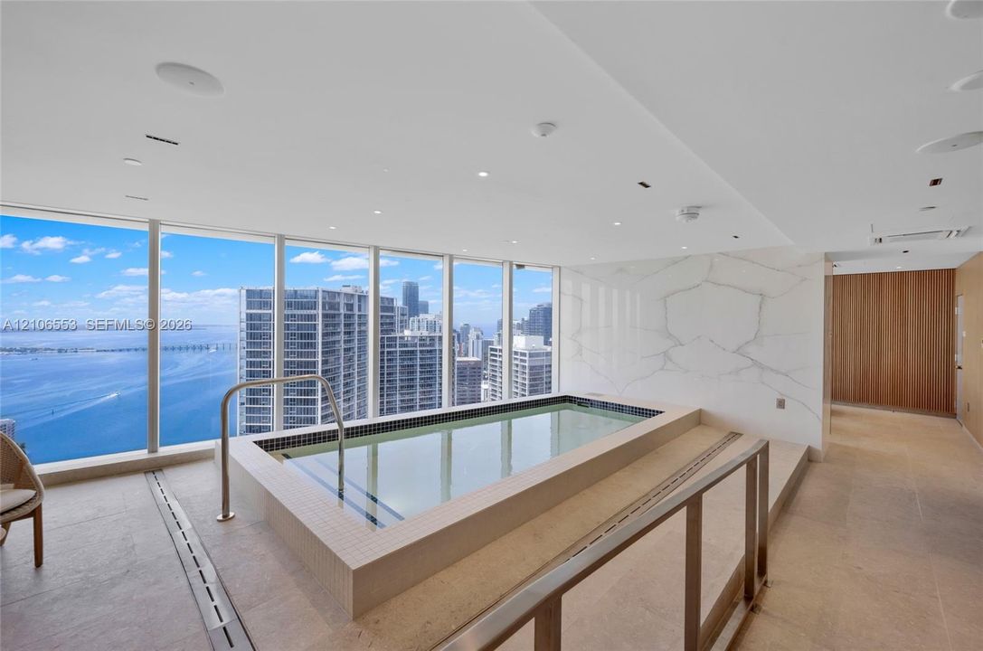 Indoor pool featuring floor-to-ceiling windows, stone-tile flooring, large-format stone wall cladding, and recessed ceiling lighting