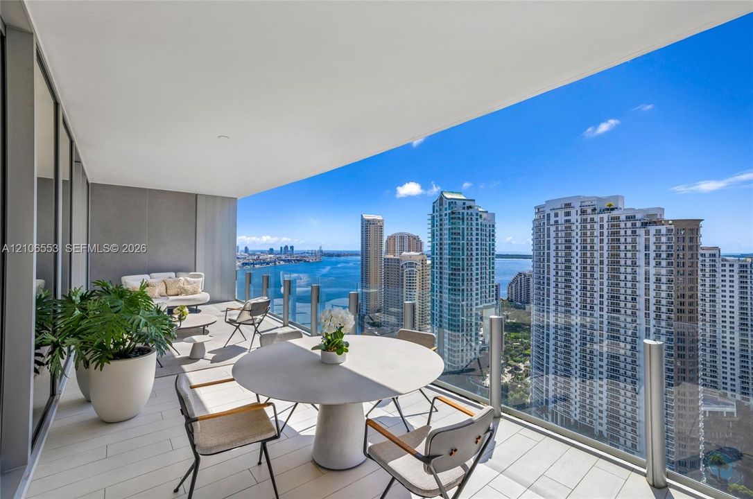 Expansive covered balcony with large-format tile flooring and a glass railing, showcasing a panorama of the surrounding urban skyline and water