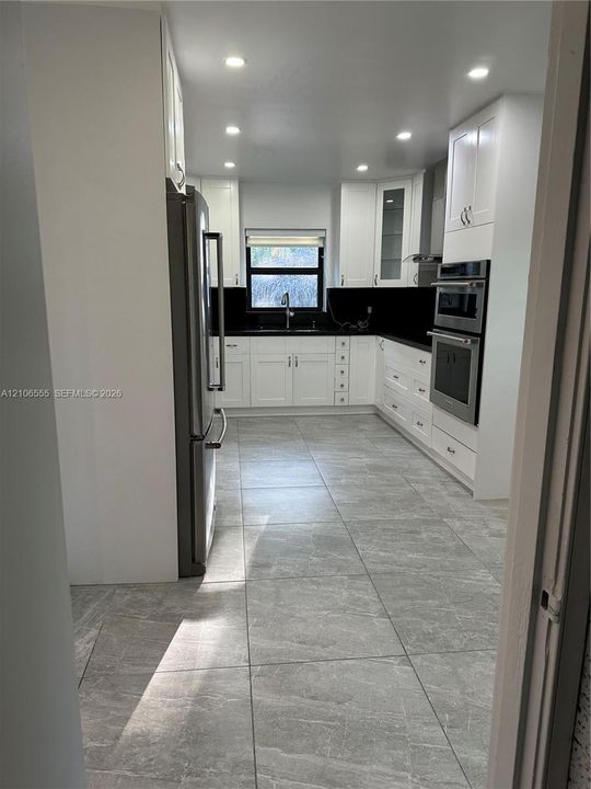 Kitchen featuring white shaker-style cabinetry, stainless steel appliances, dark stone-finish countertops, recessed lighting, and large-format tile flooring
