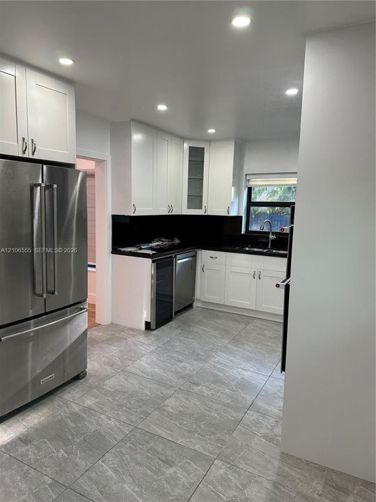 Kitchen featuring shaker-style white cabinetry, contrasting dark countertops, stainless steel appliances, integrated wine refrigerator, and stone-finish tile flooring