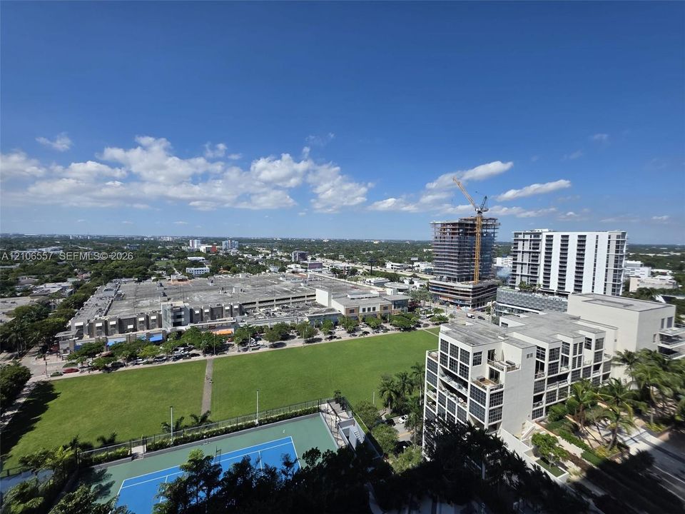 Elevated urban perspective featuring an expansive lawn area and a fenced hard-court tennis facility