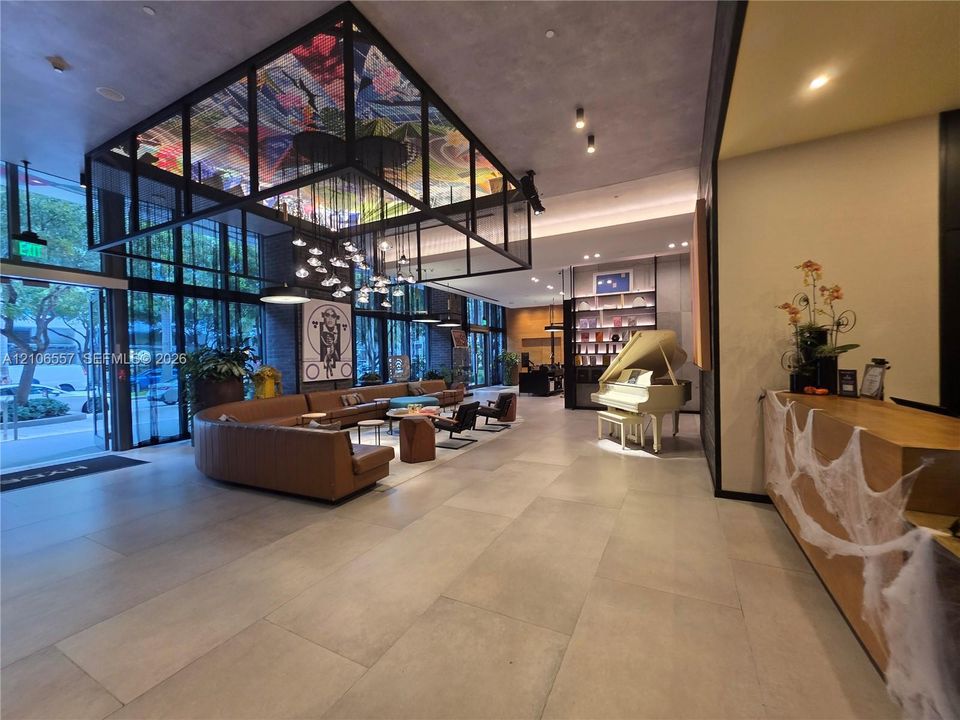 Lobby area featuring large-format tile flooring, expansive floor-to-ceiling glass windows, a custom overhead artistic installation, and built-in reception cabinetry