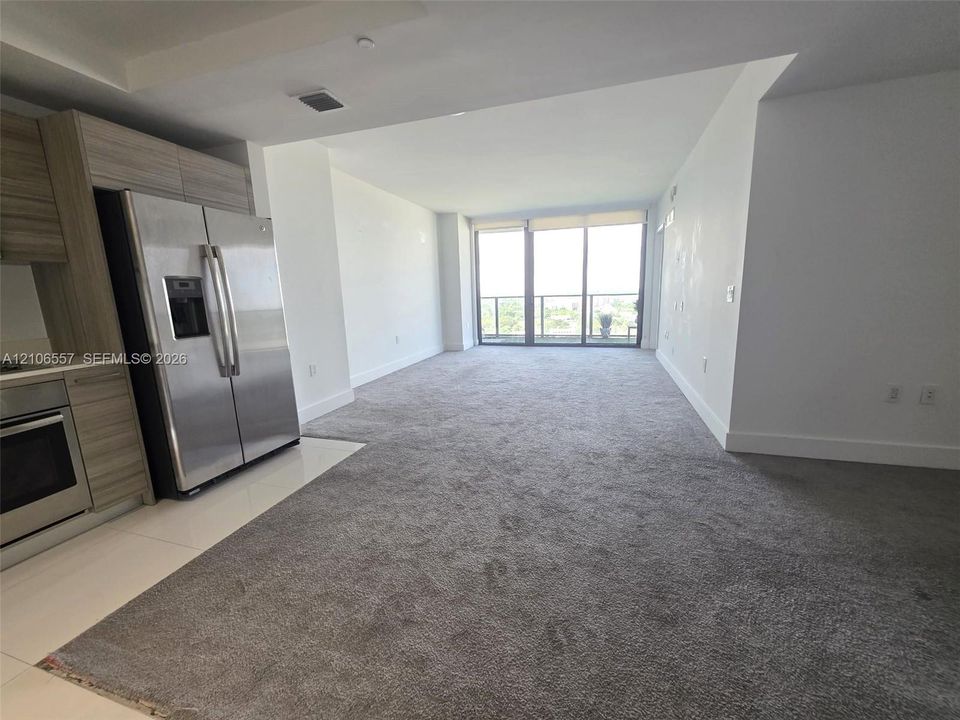 Kitchen featuring flat-panel wood-finish cabinetry, stainless steel refrigerator, built-in oven, floor-to-ceiling glass panel windows, and carpeted flooring