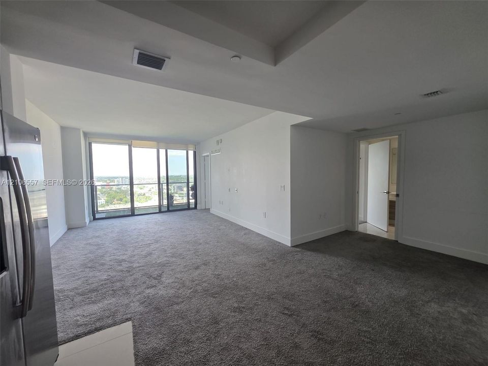 Open-concept interior featuring floor-to-ceiling glass wall, neutral wall-to-wall carpeting, recessed tray ceiling, and stainless steel kitchen appliance