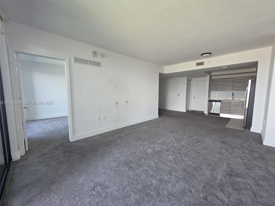 Open living area featuring wall-to-wall carpeting, kitchen with wood-finish cabinetry, stainless steel dishwasher, stainless steel refrigerator, and recessed ceiling lighting