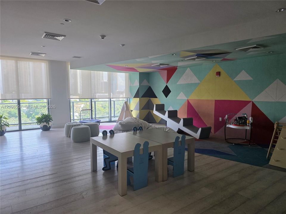 Expansive interior space featuring wood-finish flooring, floor-to-ceiling windows with roller shades, and a geometric-patterned accent wall