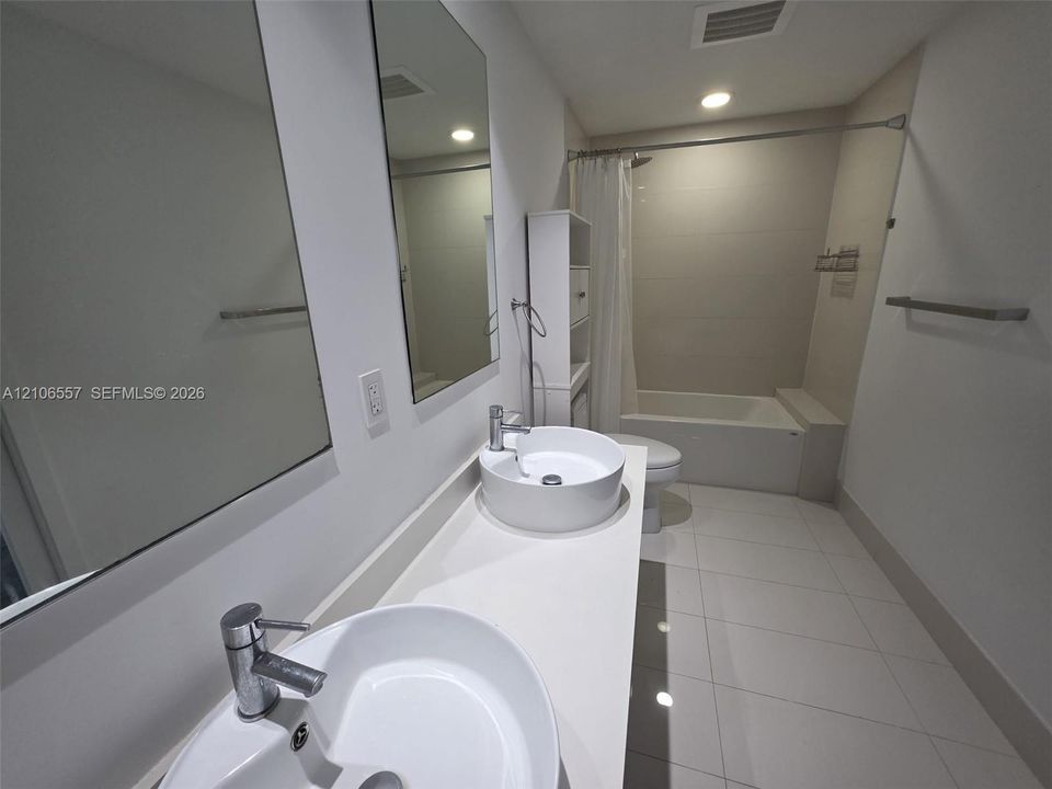 Bathroom featuring a dual-sink vanity with white countertops, vessel sinks, polished chrome faucets, large vanity mirrors, and neutral tile flooring