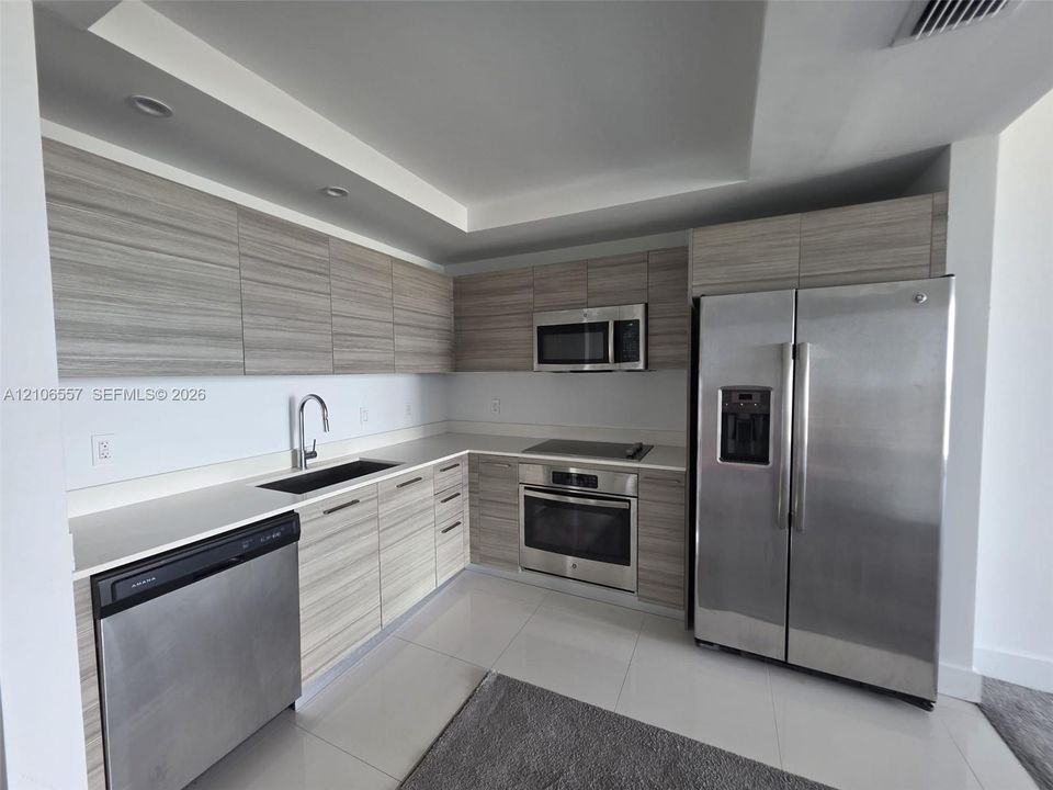 Kitchen featuring horizontal grain wood-finish cabinetry, solid surface countertops, recessed lighting, and stainless steel appliances