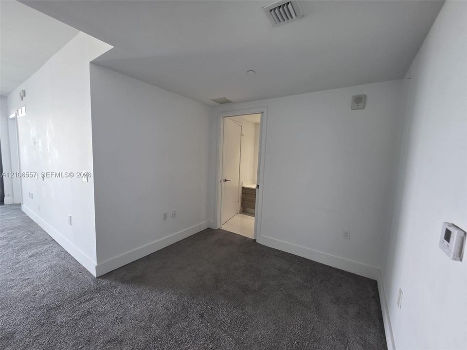 Interior space featuring wall-to-wall carpeting, smooth white walls, recessed ceiling lighting, and a doorway revealing a vanity with wood-finish cabinetry