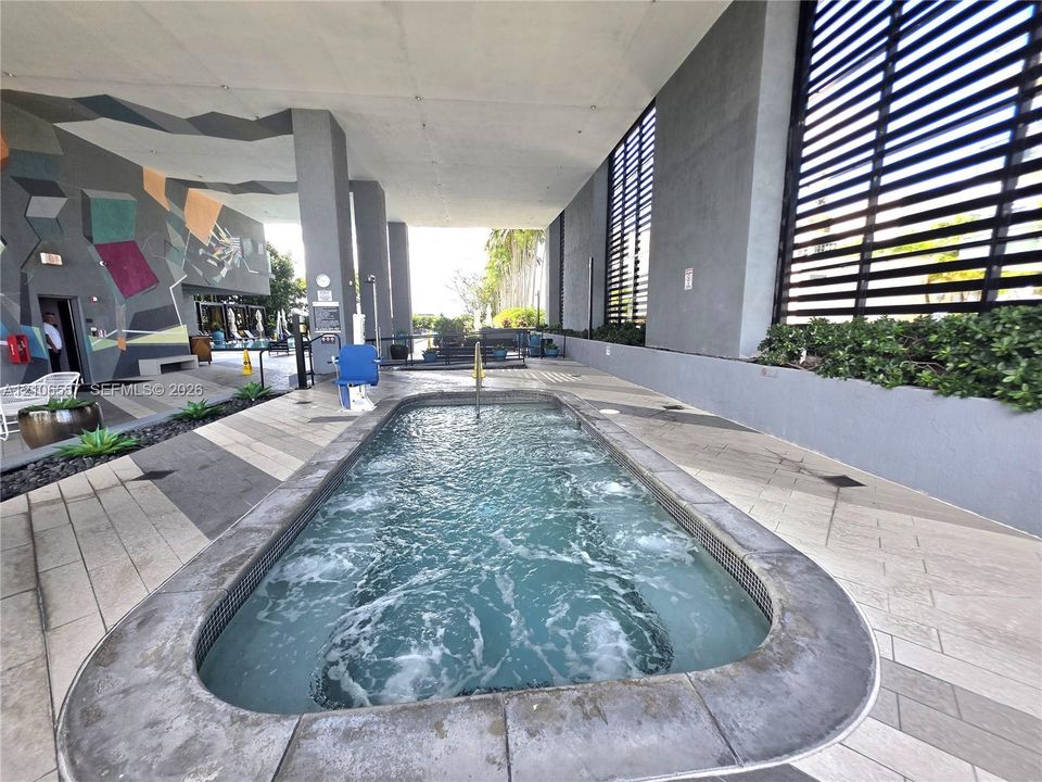 Covered spa featuring a concrete surround, geometric wall mural, integrated horizontal slat privacy screen, and patterned tile flooring