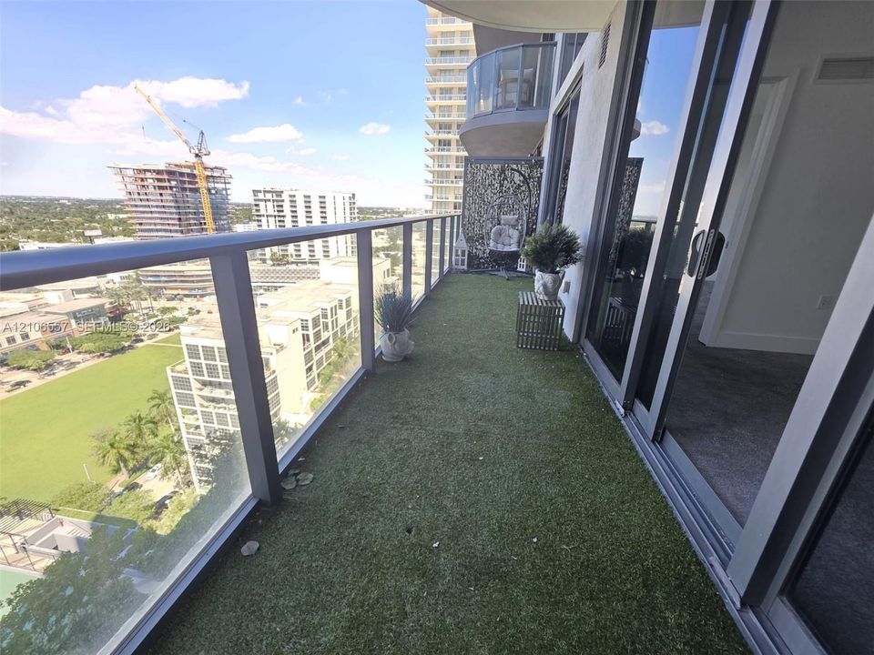 Covered balcony featuring artificial turf flooring, a metal and glass railing, and oversized sliding glass doors