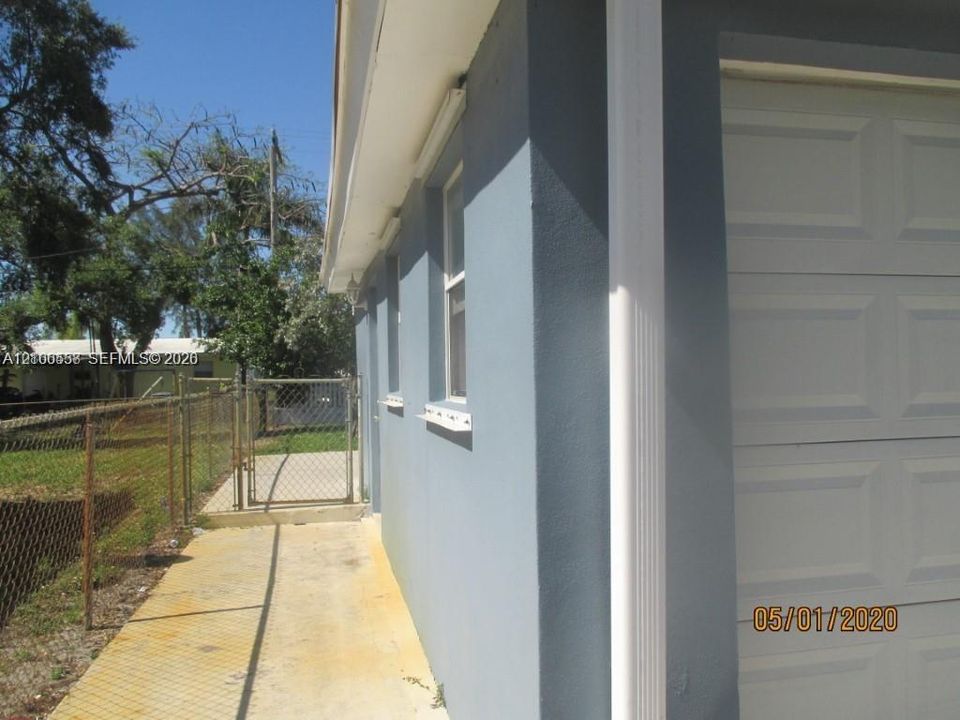 Exterior side profile featuring smooth stucco siding, white gutter downspouts, inset windows, and a chain-link fenced perimeter