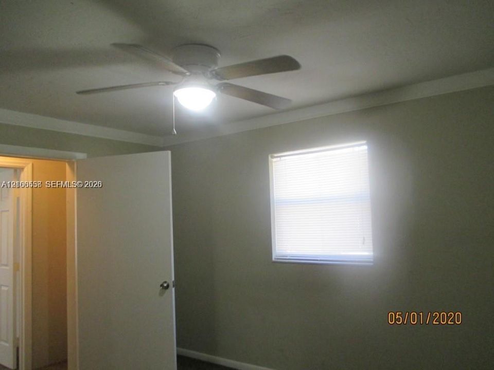 Room featuring a ceiling fan with integrated lighting, a single-panel interior door, and a window with horizontal blinds