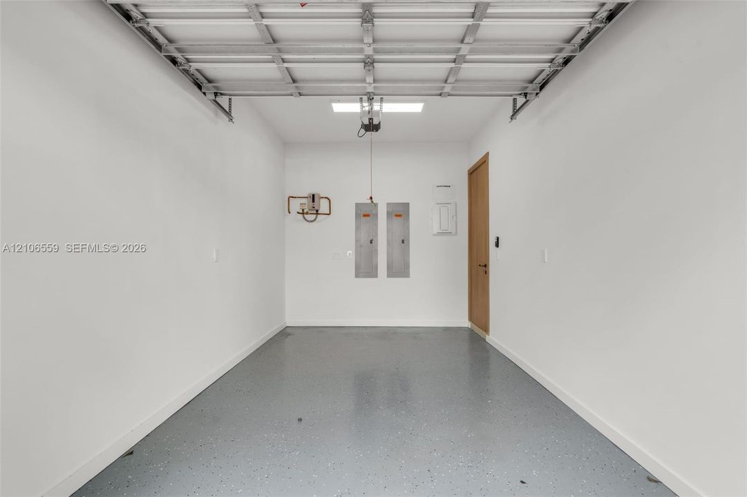Enclosed garage featuring a durable epoxy-coated floor, white painted walls, a sectional metal door, and a built-in flush-mount lighting fixture