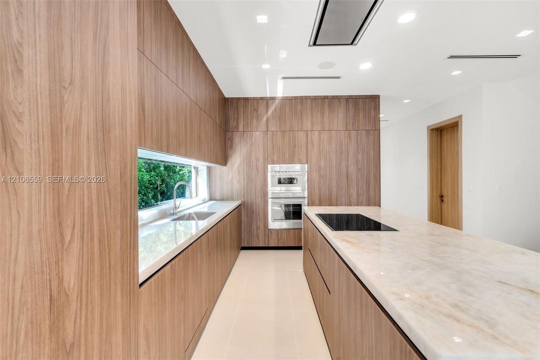 Kitchen featuring full-height wood-finish cabinetry, stone countertops, integrated induction cooktop, built-in double oven, and horizontal window