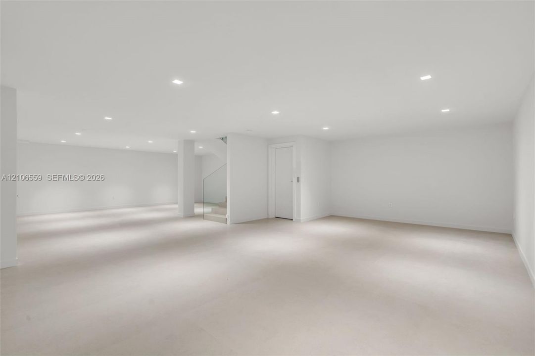 Open floor plan featuring recessed lighting, smooth finish flooring, neutral wall color, and a structural staircase with a glass panel railing