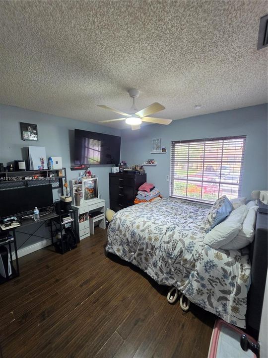 Room featuring wood-finish flooring, a ceiling fan with integrated light, and a window with horizontal blinds