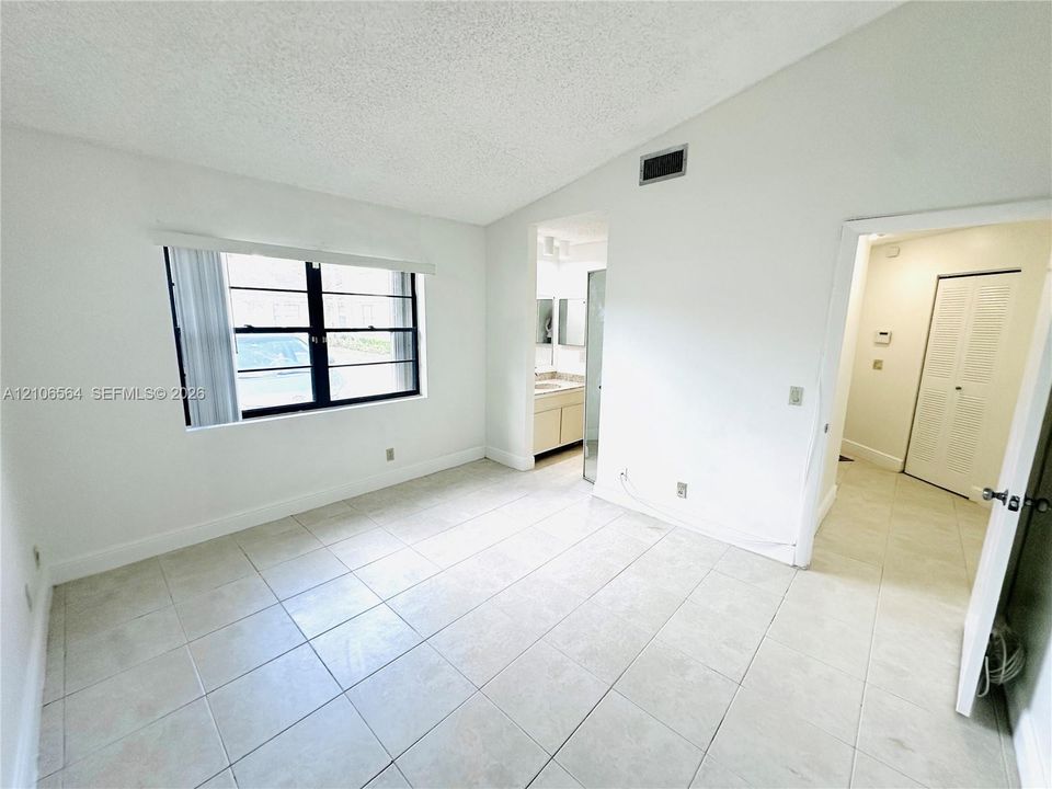 Room featuring vaulted ceilings, neutral ceramic tile flooring, and a window with black-framed casing