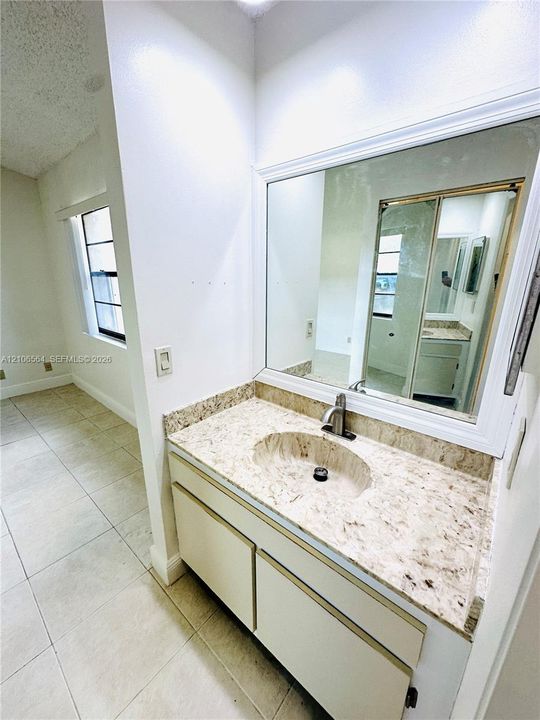 Vanity featuring stone-finish countertop, undermount sink, single-handle faucet, large wall-mounted mirror with white trim, and neutral tile flooring