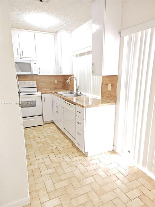Kitchen featuring white cabinetry, wood-finish countertops, stainless steel sink with a high-arch faucet, white built-in appliances, and herringbone-patterned tile flooring
