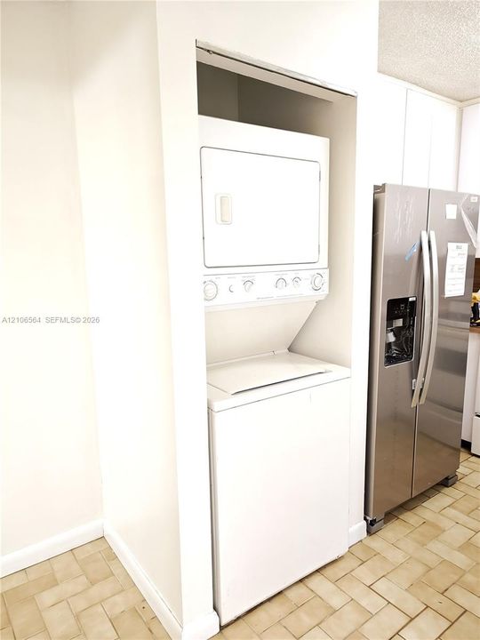 Built-in white stackable laundry unit, stainless steel side-by-side refrigerator, and tile flooring