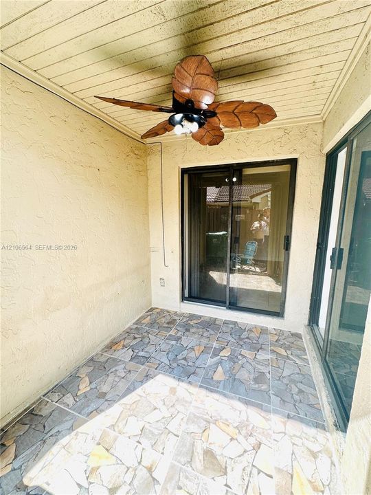 Covered patio featuring multi-tonal stone-tile flooring, beadboard ceiling, and a decorative leaf-blade ceiling fan with integrated lighting