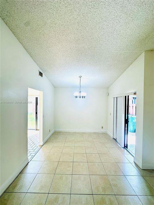 High-ceilinged room featuring neutral tile flooring, a multi-bulb overhead chandelier, and sliding glass door access to the exterior