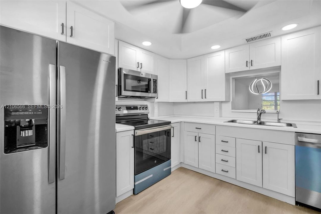 Kitchen featuring white shaker-style cabinetry, solid-surface countertops, recessed lighting, and stainless steel appliances