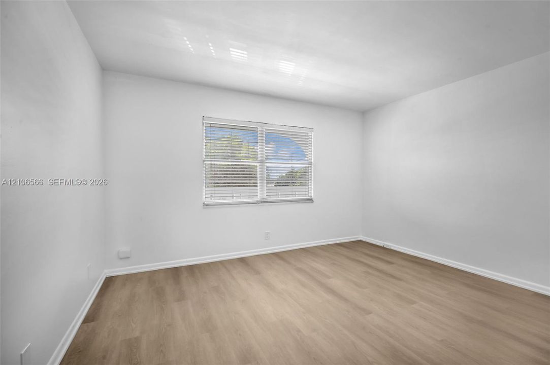 Neutral-toned interior space featuring wood-finish flooring, white walls, and a multi-pane window with integrated blinds