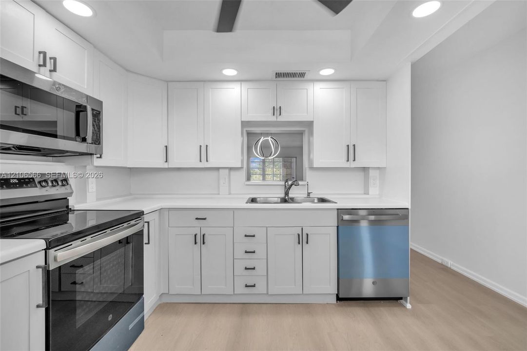 Kitchen featuring white shaker-style cabinetry, solid-surface countertops, recessed lighting, and stainless steel appliances