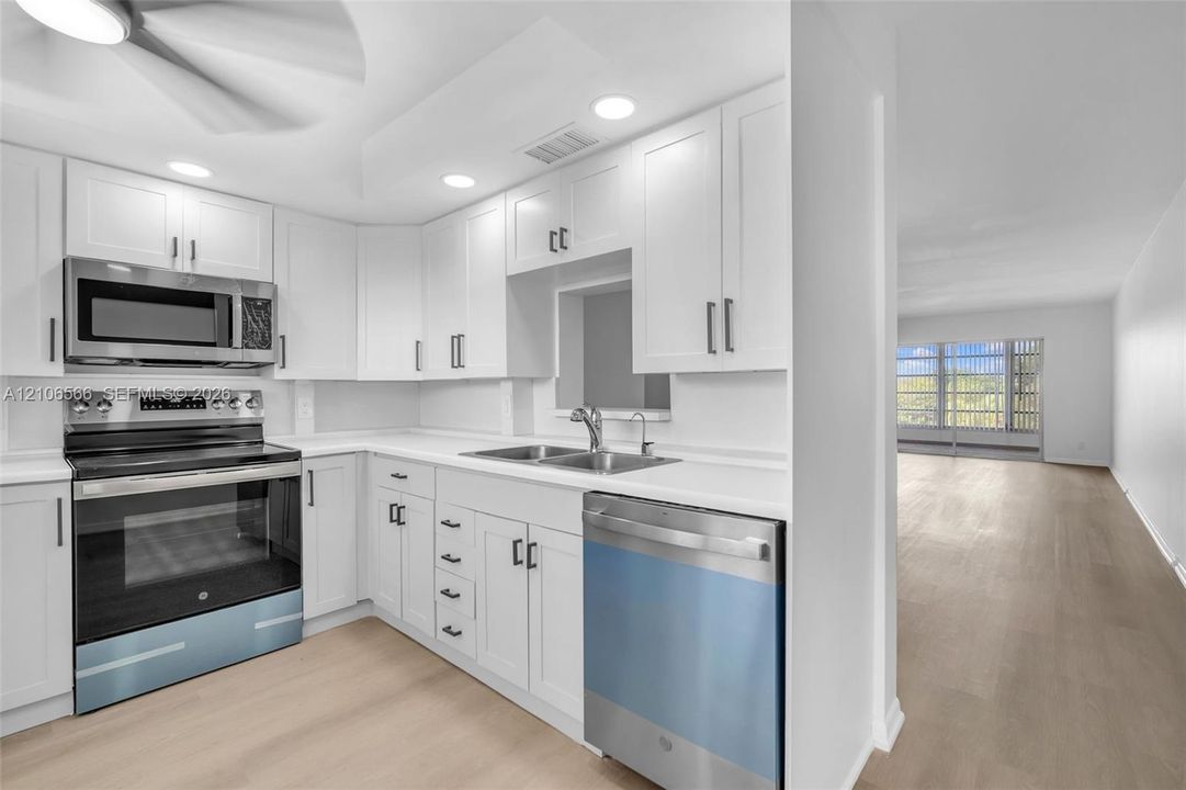 Kitchen featuring white shaker-style cabinetry, stainless steel appliances, solid-surface countertops, recessed lighting, and wood-finish flooring