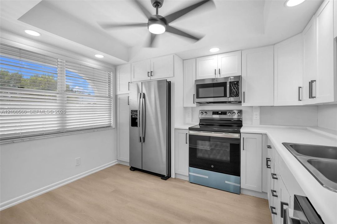 Kitchen featuring white cabinetry, solid-surface countertops, stainless steel appliances, wood-finish flooring, and a tray ceiling with a center-mount fan