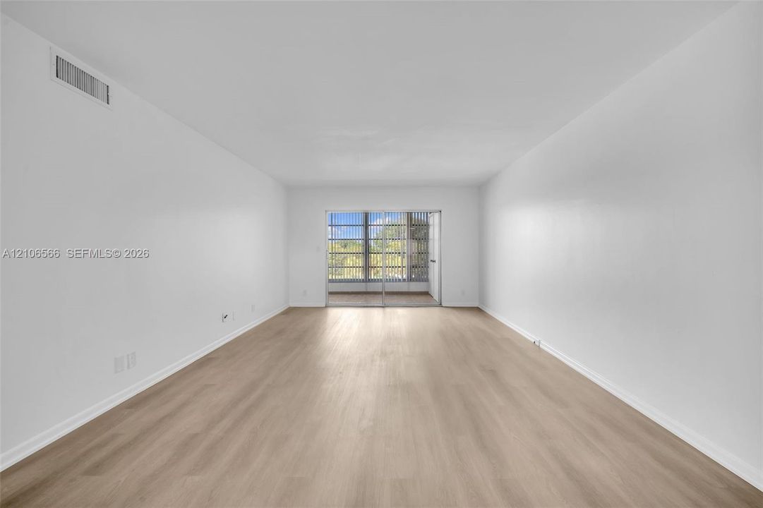 Spacious room featuring wood-finish flooring and floor-to-ceiling sliding glass doors leading to a private outdoor balcony
