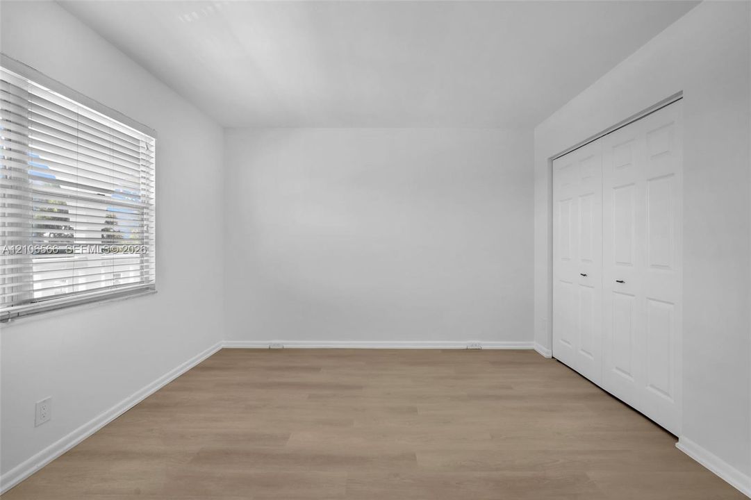 Room featuring wood-finish flooring, white walls, horizontal window blinds, and a double-panel closet