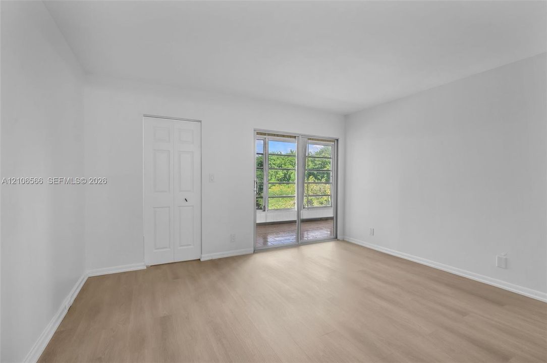 Neutral-toned interior space featuring light-colored wood-finish flooring, white walls, a multi-panel closet door, and sliding glass doors