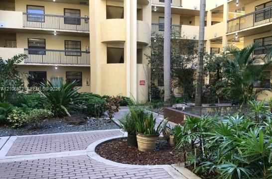 Multi-story building exterior featuring a central courtyard with paved brick walkways, a water feature, and mature tropical landscaping
