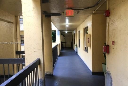 Covered exterior corridor featuring textured stucco walls, solid structural pillars, and dark-finished metal railings