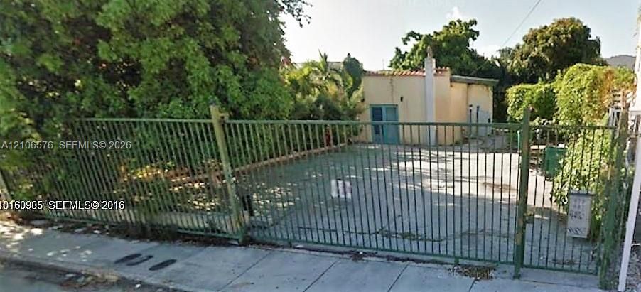 Gated exterior featuring a paved driveway, metal perimeter fencing, and mature landscaping