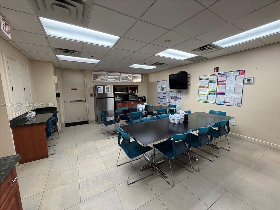 Breakroom featuring a built-in wood-finish cabinetry counter with dark stone-surface countertops, tile flooring, and integrated recessed lighting