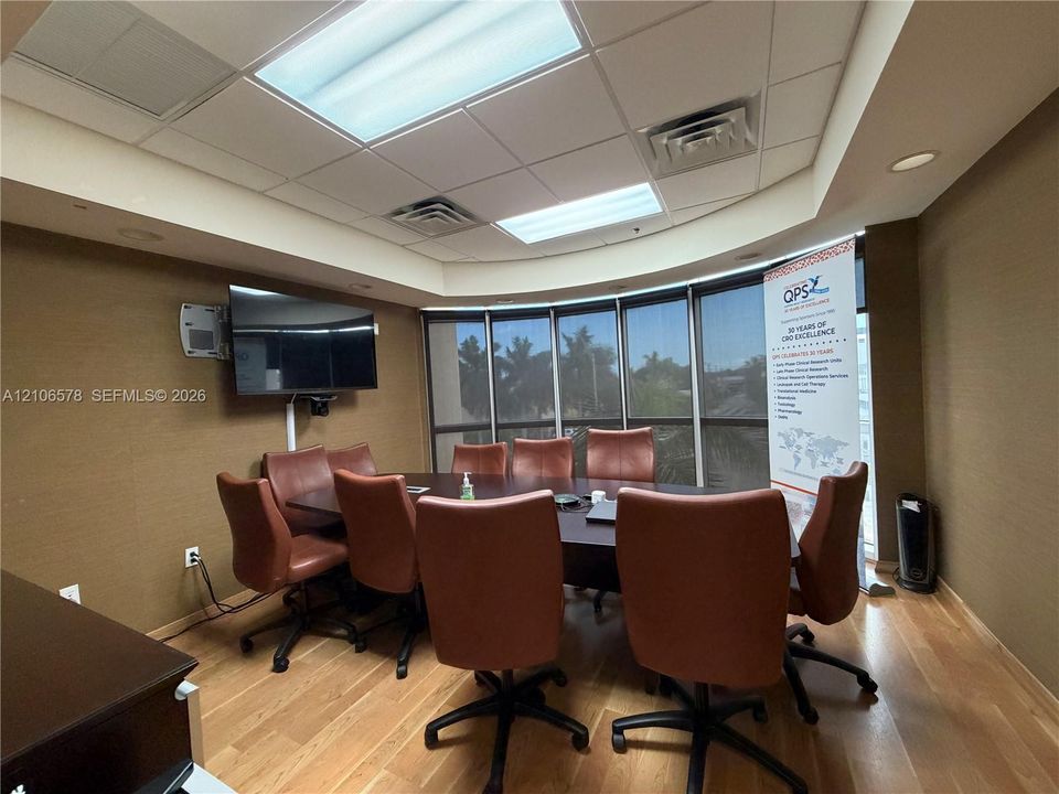 Conference room featuring wood-finish flooring, drop ceiling with recessed lighting, curved window wall, and wall-mounted monitor