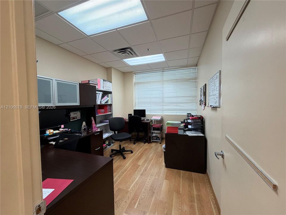 Enclosed room featuring wood-finish flooring, built-in cabinetry, drop-ceiling panels, and a large window with horizontal blinds