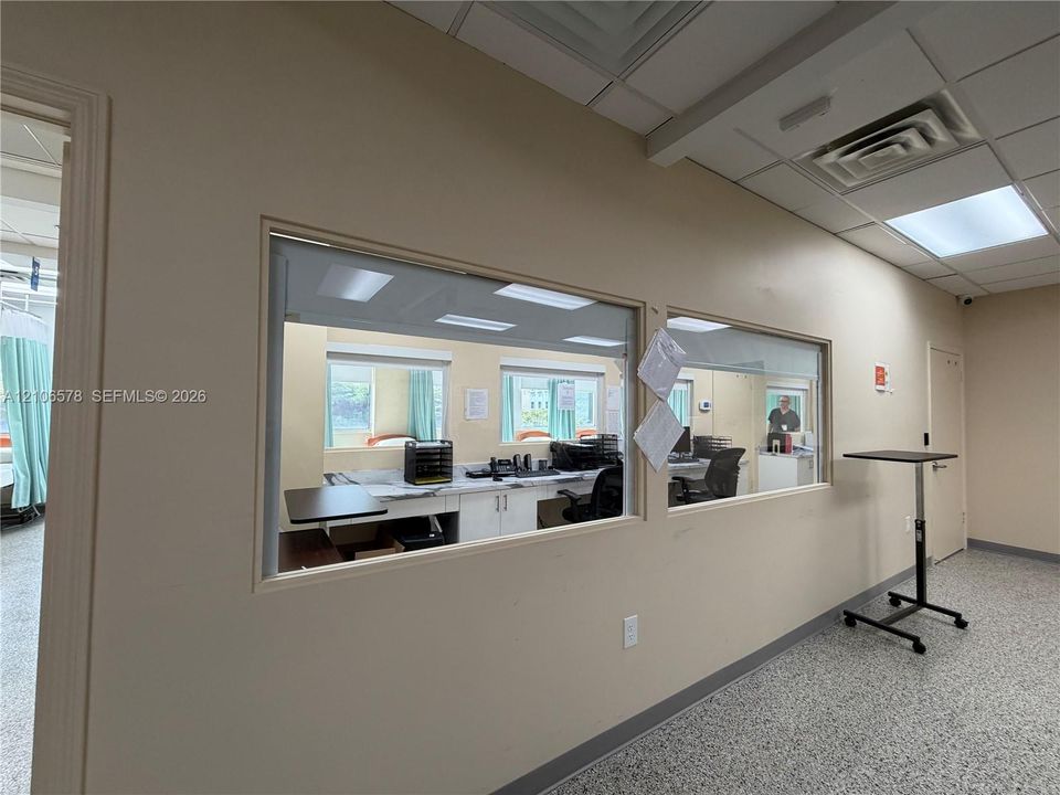 Interior wall featuring dual integrated glass partition windows, white cabinetry with stone-finish countertops, drop ceiling grid, and seamless flooring