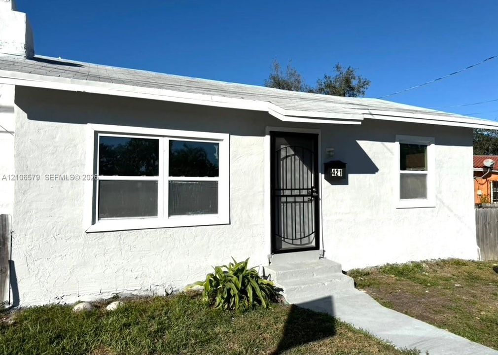 Stucco exterior facade featuring a covered entryway, white-framed windows, concrete front steps, and a decorative metal storm door