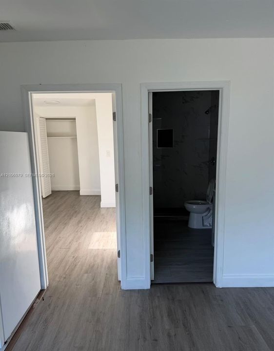 Wood-finish flooring throughout, featuring two doorway entrances with crisp white trim and a walk-in closet with built-in shelving