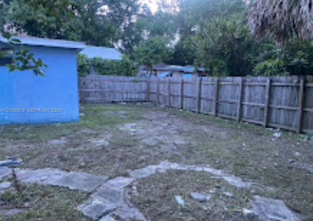 Rear outdoor area featuring a wood fence, flagstone pathways, and mature trees