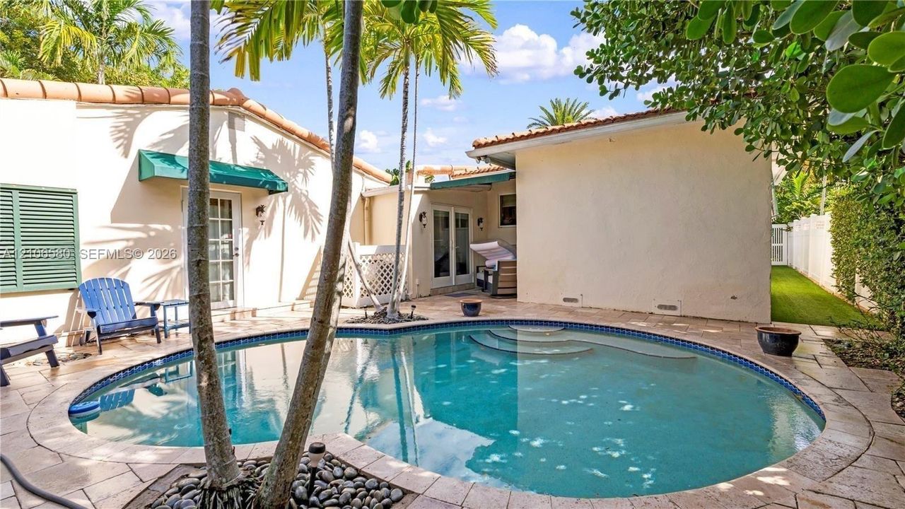 Exterior courtyard featuring a curved swimming pool, natural stone pool deck, built-in steps, and palm trees