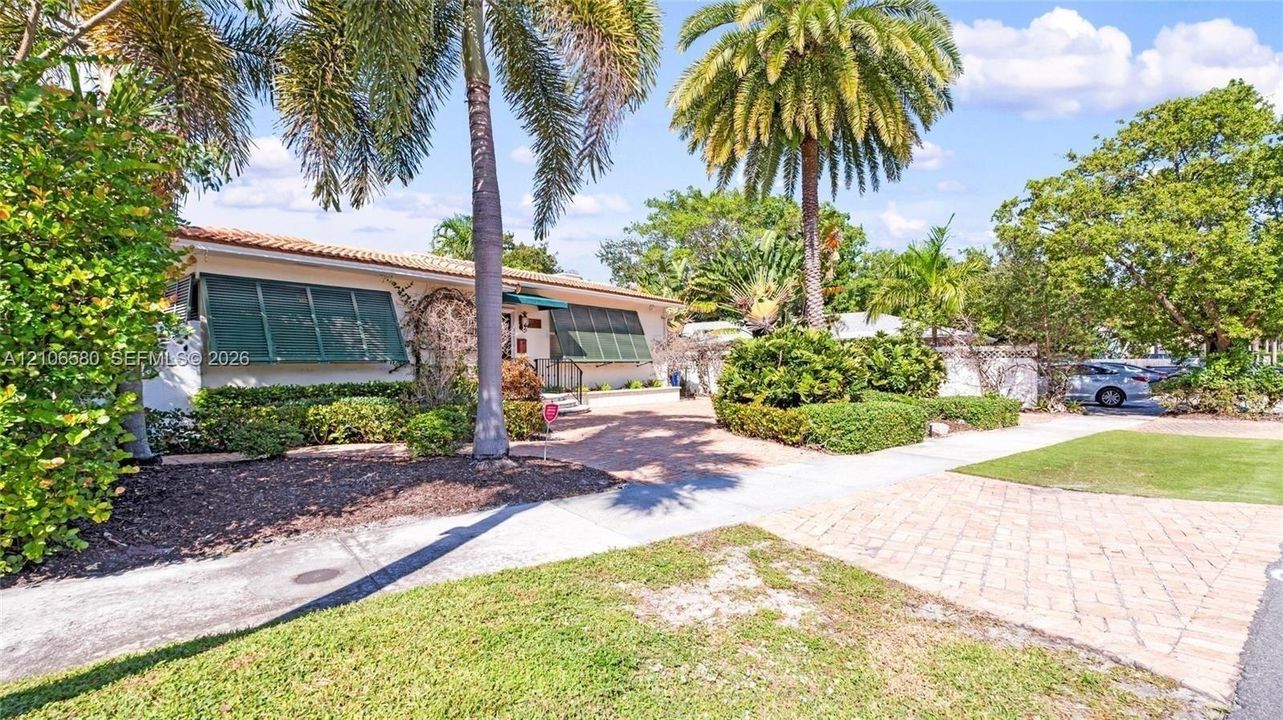 Single-story residence featuring a tile roof, decorative green shutters, paver driveway, and mature landscaping