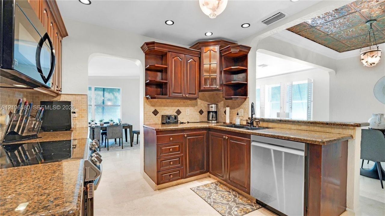Kitchen featuring stained wood cabinetry, stone countertops, stone tile backsplash, recessed lighting, and a decorative ceiling inlay