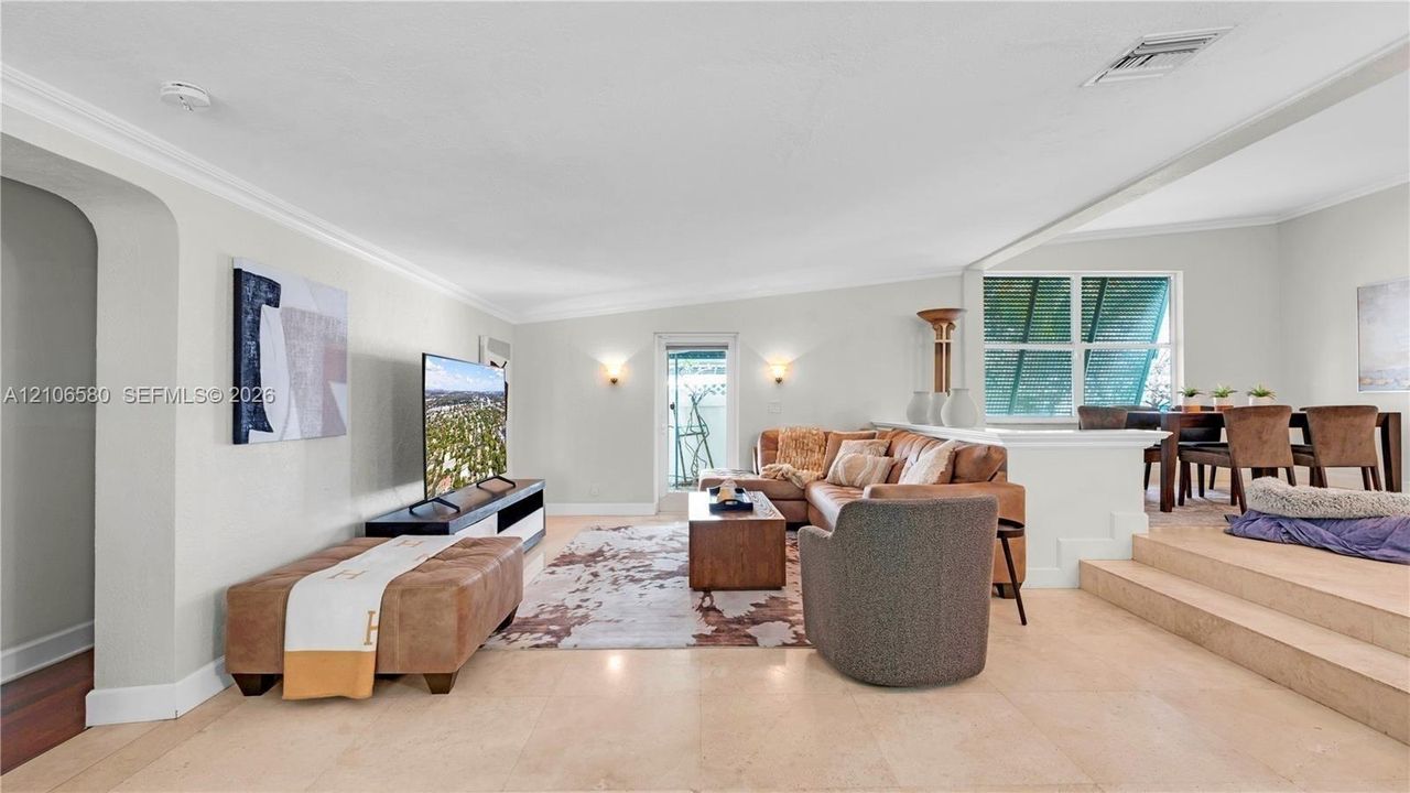 Open-concept floor plan featuring light-toned tile flooring, recessed crown molding, arched entryways, and a multi-level layout with a carpeted elevated platform