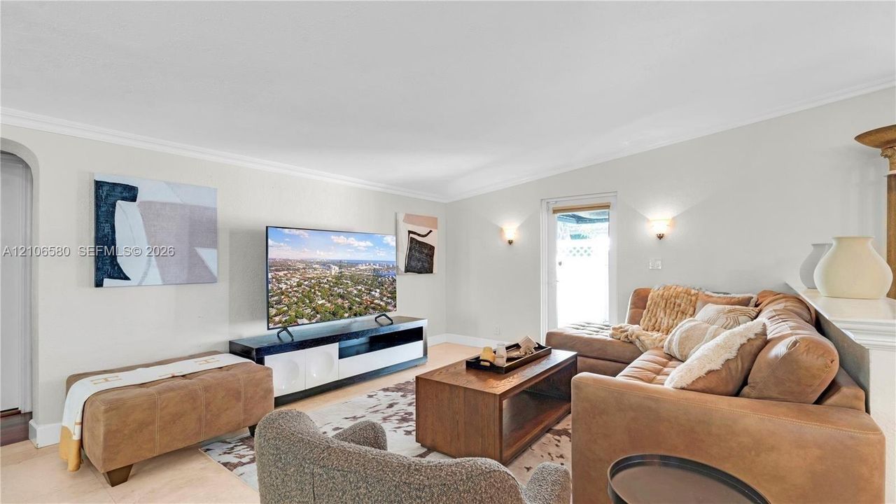 Living space featuring neutral wall paint, arched entry, crown molding, and wall-mounted sconce lighting